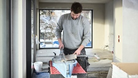 Ein Mann schneidet eine graue Fliese an einem Fliesenschneidegerät. 
