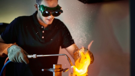 Person schmiedet mit Schutzausrüstung ein Werkstück