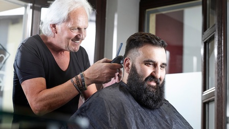 Ein älterer Friseur rasiert einem Kunden den Nacken aus. 