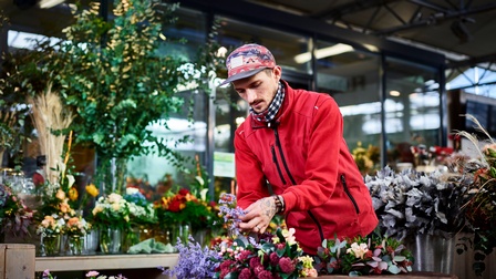 Ein junger Mann in einer Gärtnerei bereitet violette Blumen für Sträuße vor