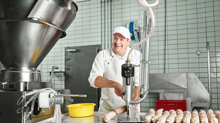 Lächelnde Person in industrieller Küche bei der Herstellung von Würsten