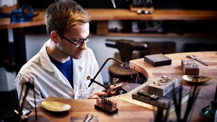 Ein junger Mann sägt in der Werkstatt an einem Goldring