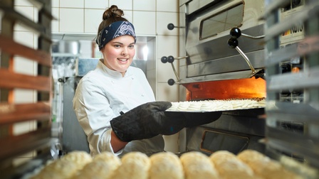 Eine junge Konditorin holt ein Blech frisches Baiser aus dem Ofen