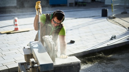 Ein Mann sägt einen Pfasterstein zurecht, sodass er verlegt werden kann