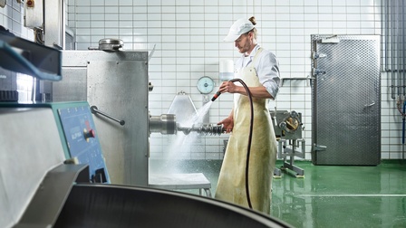 Person reinigt Maschinen in einem Fleischereibetrieb