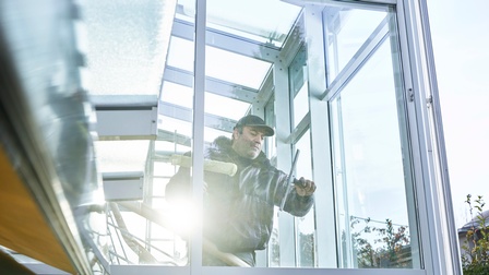 Ein Mann putzt eine Scheibe in einer weiten Glasfront von innen mit einem Abzieher