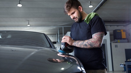 Ein junger Karosseriebautechniker poliert eine Autokarosserie in einer Garage