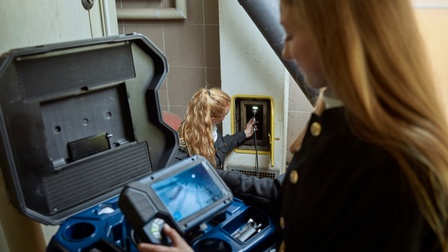 Person im Vordergrund verschwommen bedient Gerät, zweite Person im Hintergrund führt Kabel mit Lampe in Kaminschacht