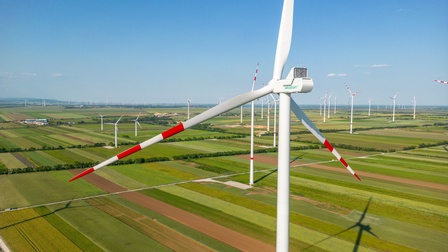 Fokus auf Windrad mit rotweißroten Spitzen auf Feld mit weiteren Windrändern stehend unter blauem Himmel