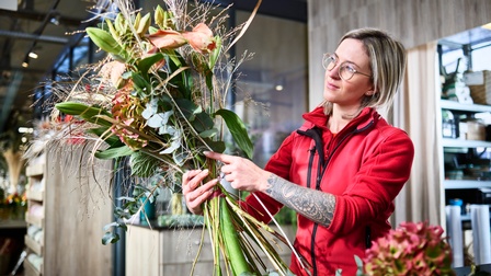 Eine junge Frau bindet einen Strauß Blumen zu einem Gesteck in einer Gärtnerei
