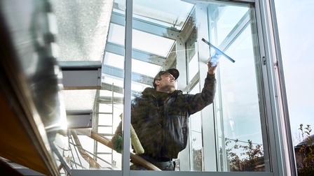 Ein Mann putzt eine Fensterfront von innen mit einem Abzieher