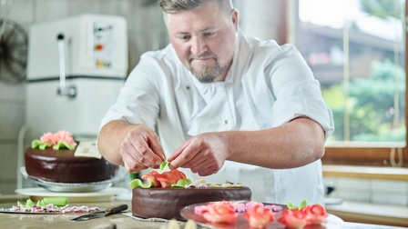Ein Konditor schmückt Schokoladenkuchen mit Marzipanblüten