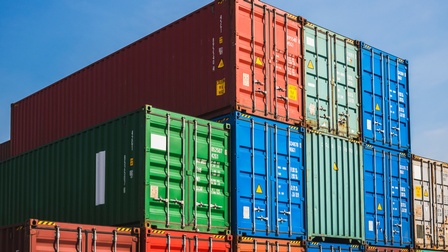 Viele Container in unterschiedlichen Farben stehen in mehreren Stapeln nebeneinander unter blauem Himmel.