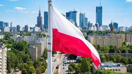 Die polnische Flagge weht im Wind, im Hintergrund eine Stadtansicht.