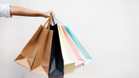 Ein ausgestreckter Arm hält mehrere Einkaufstaschen in der Hand