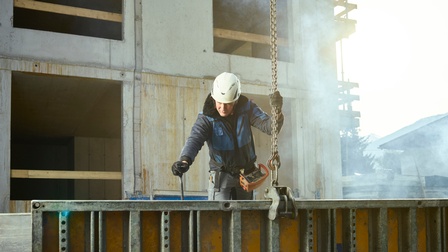 Ein Mann platziert mithilfe eines Krans eine Betonverschalung am Rohbau