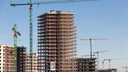 Mehrere Rohbauten von hohen Gebäuden mit vielen Stockwerken unter blauem Himmel. Zwischen den Gebäuden stehen versetzt viele Kräne.