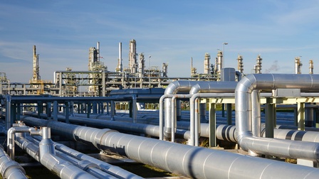 Viele Pipelines verlaufen parallel nebeneinander zu einer Raffinerie hin. Der Himmel ist blau