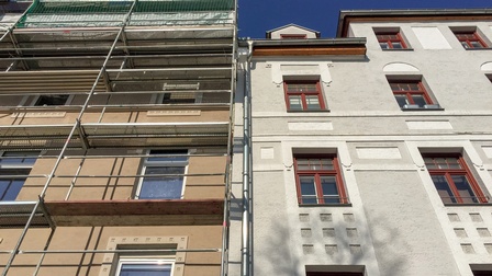 Die Fassaden zweier Altbaugebäude direkt nebeneinander. Vor der Fassade des linken Hauses ist ein Baugerüst. Über den Gebäuden ist der blaue Himmel