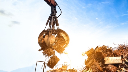 Schrott, der in dämmrigen Sommerlicht von einer Baggerzange aufgelesen wird
