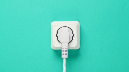 Detailansicht eines weißen Netzteils mit Kabel, das in Steckdose steckt auf türkisblauem Hintergrund