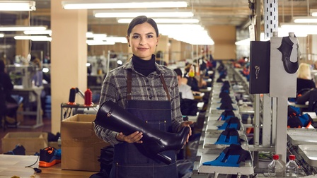 Eine Frau in einer Schuhfabrik hält einen Lederstiefel in den Händen
