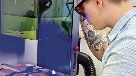 Rückenansicht einer Person mit Schutzbrille, die an einem 3D-Drucker steht