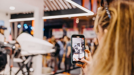 Eine junge Frau fotografiert mit ihrem Handy den Messestand der AUSSENWIRTSCHAFT AUSTRIA