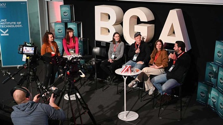 Interview vor einer Kamera mit sechs Menschen. Dahinter groß der Schriftzug BGA