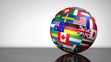 Nahaufnahme einer Weltkugel, die auf einem schwarzen Tisch liegt. Auf der runden Kugel sind Flaggen als Rechtecke abgebildet. Die Weltkugel wirft einen Schatten auf dem Tisch, der Hintergrund ist weiß. 