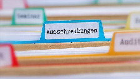 Nahaufnahme mehrerer, brauner, horizontal stehender Mappen, in denen weiße Zettel sind. An jeder Mappe ist ein Etikett angebracht, auf dem ein Wort steht. Auf einem steht Ausschreibungen