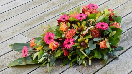 Blumengesteck mit vorwiegend rosa und orangen Blüten auf Holzboden platziert