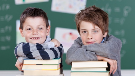 Glückliche Kinder mit Büchern in einer Schule vor einer grünen Tafel in einem Klassenzimmer