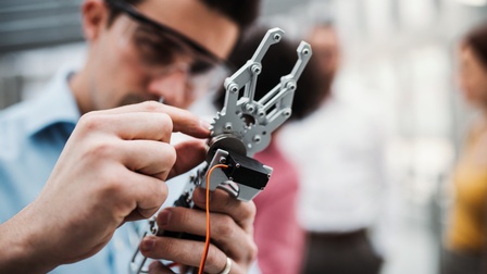 Person mit Schutzbrille bedient einen Roboterarm, Close-up