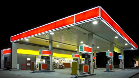 Außenaufnahme einer Tankstelle bei Nacht mit einem rot leuchtenden Dach. Unter dem Dach sechs Säulen, an jeder Säule sind Zapfhähne montiert.