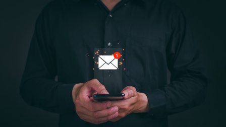 Frontale Aufnahme einer Person, die ein Smartphone hält. Über dem Smartphone ist ein Icon eines Briefumschlags. An der rechten oberen Ecke des Briefumschlags ist eine weiße eins in einem roten Kreis