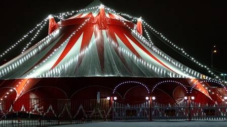 Außenaufnahme eines beleuchteten rot-weißen Zirkuszeltes bei Nacht