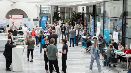 Mehrere Personen finden sich im Foyer bei einer Messe und holen sich an den Ständen ihre Infos