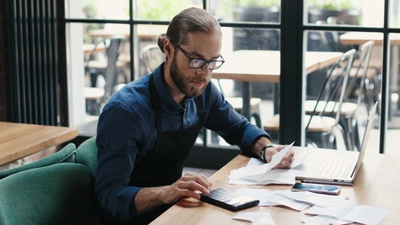 Person mit Brille sitzt an einem Schreibtisch und arbeitet mit einem Laptop