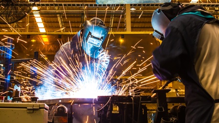 Zwei Personen in Schutzkleidung beim Schweißen, Funken sprühen.