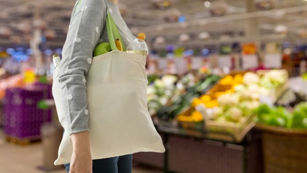 Detailansicht einer Person mit voller Einkaufstasche um die Schulter gehängt in Superparkt stehend