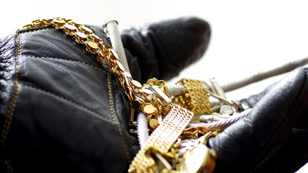 Ketten aus Gold und weitere Schmuckstücke werden von einem schwarzen Handschuh gehalten