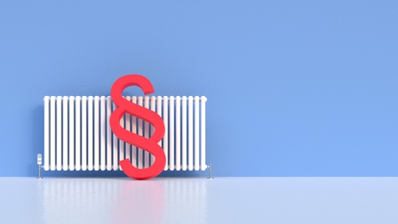 Rotes Paragrafenzeichen lehnt an Heizkörper vor blauer Wand