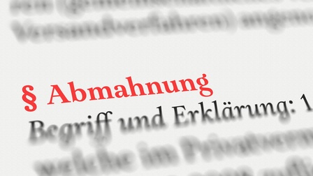 Nahaufnahme eines Textes mit Definition zum Thema Abmahnung inklusive Paragraphenzeichen in roter Schrift, weiterer Text in schwarzer Farbe zeigt sich verschwommen
