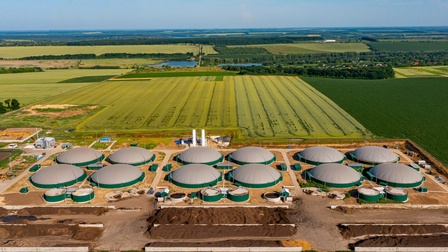 Große runde Biogastanks in Erdfeldern umgeben von grünen Feldern unter blauem Himmel