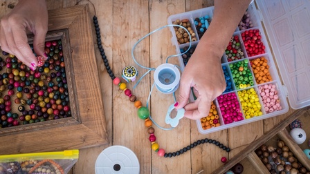 Hände, die mit kleinen, bunten Steinen Schmuck herstellen