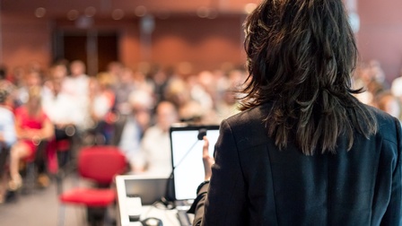 Rückansicht von einer vortragenden Person in einem vollen Konferenzraum