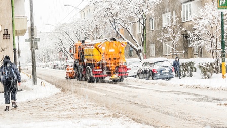 Ein Schneeräumungsfahrzeug räumt den Schnee auf den Straßen bei starkem Schneefall, auf den Gehwegen befinden sich Leute.