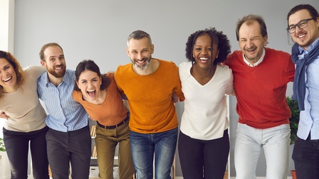 Mehrere Personen stehen gemeinsam freudig in einem Büroraum in einer Reihe.
