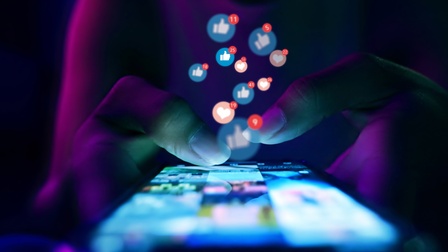 Finger einer Frau berührt die Scroll‑Seite einer App auf dem Smartphone. In einem Raum mit blau‑violetten Neonfarben. Konzept: Social Media, Marketing, Like‑Buttons.